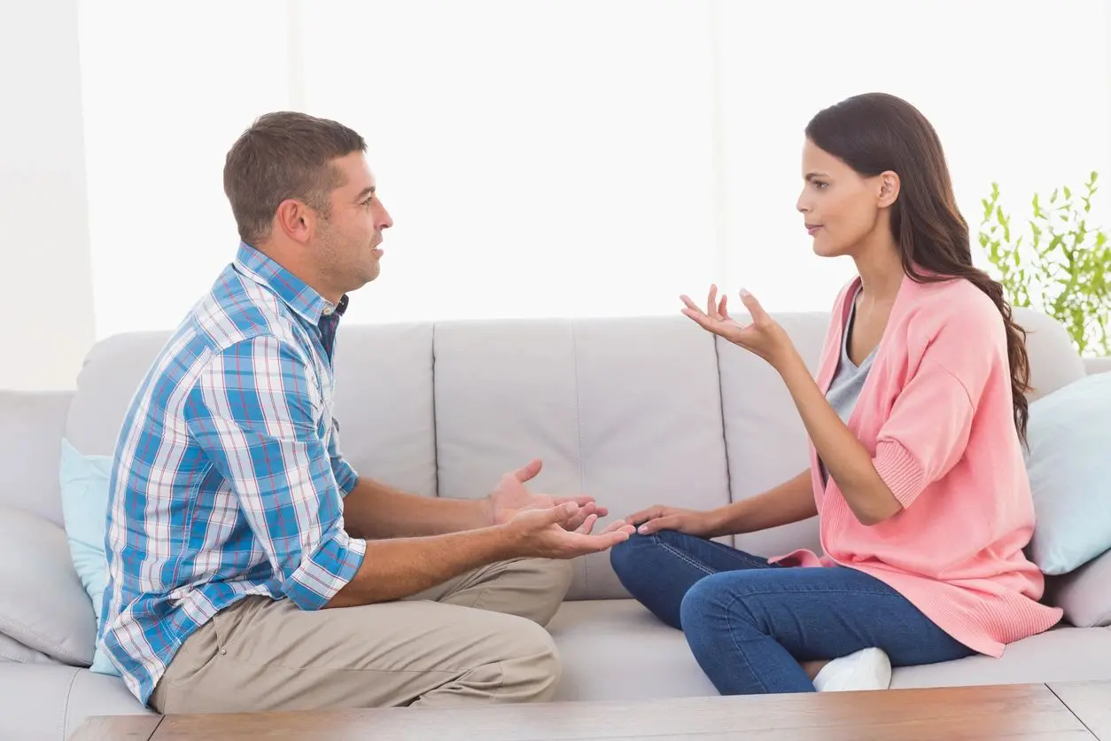 A man and woman sitting on the couch talking.