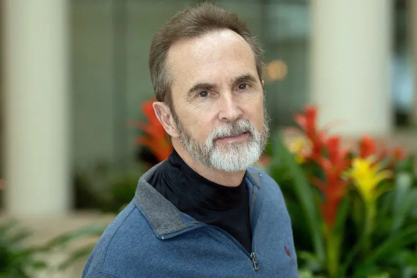 Portrait of a mature man with gray hair and beard, wearing a blue jacket.