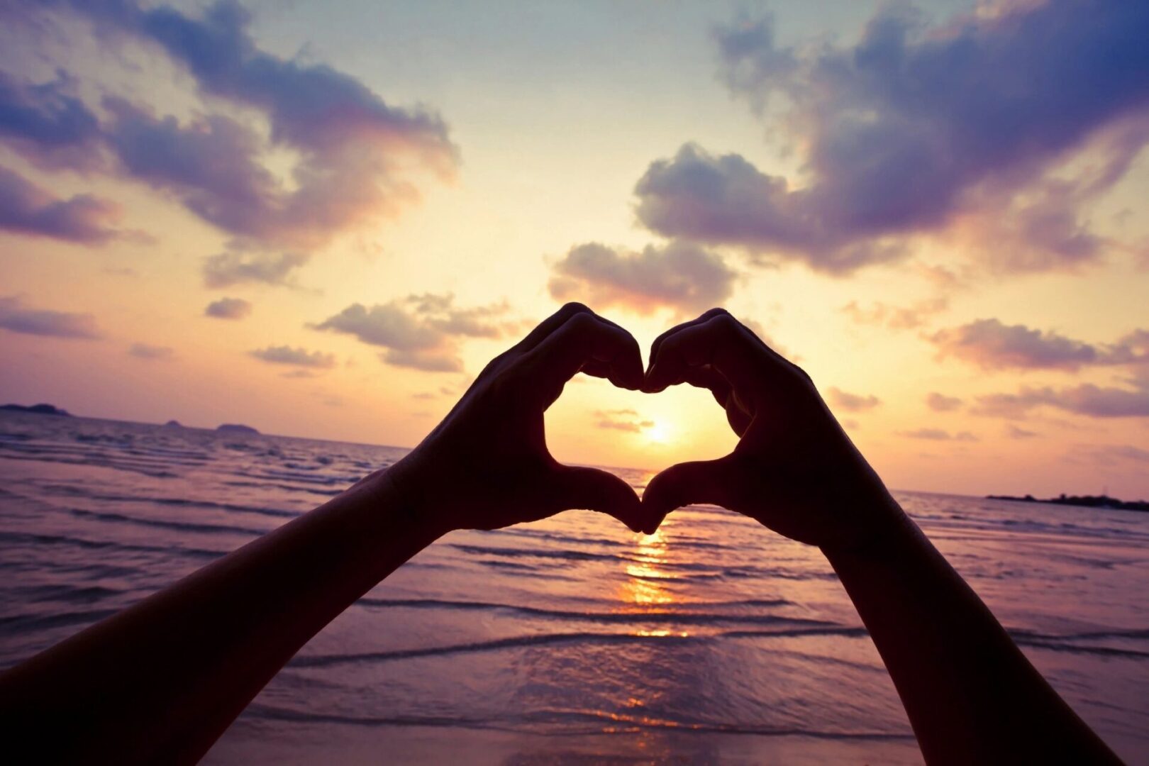 A person 's hands are in the shape of heart at sunset.